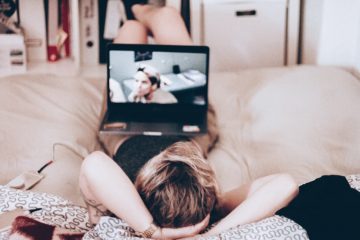 woman lying on bed while watching tv